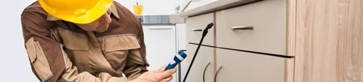 Roach exterminator applying treatment under kitchen cabinets in Madison, WI