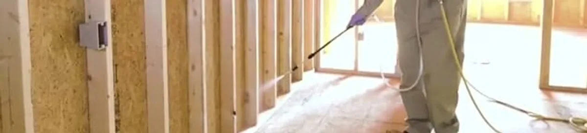 Termite treatment technician applying spray along framing and unfinished walls in Madison, WI